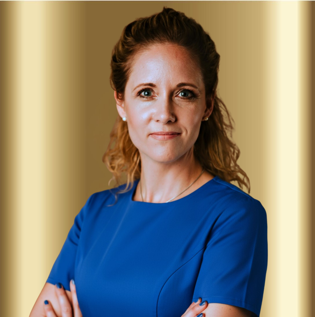 A portrait of a confident woman with curly hair wearing a blue dress, standing with her arms crossed against a golden background.